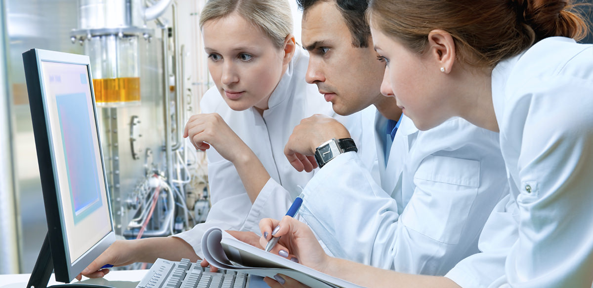 Three scientists standing at a desk and looking at a packet of papers