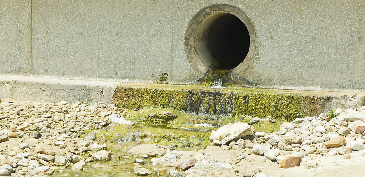 Water pouring out of the opening of a storm sewer pipe and into some type of body of water